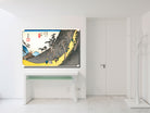 A framed art print of a Japanese ukiyo-e woodblock scene, depicting a mountain landscape with figures, displayed on a white wall above a white console table in a minimalist room.