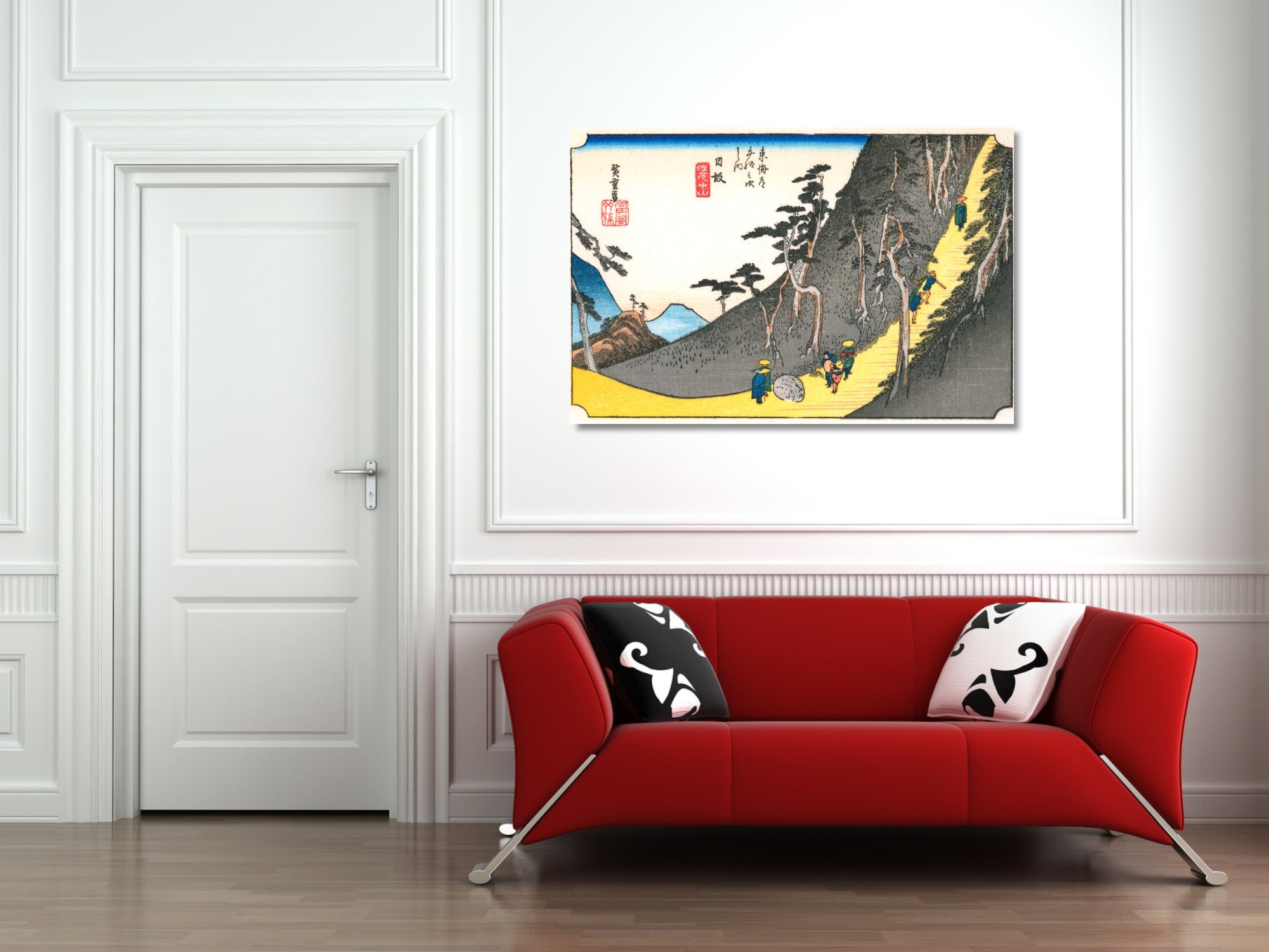 A framed Japanese-style art print hangs on a white paneled wall above a modern red sofa with black-and-white pillows in a bright room.