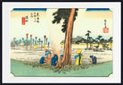 A framed Japanese-style art print showing a landscape scene with a large tree, figures near the base, distant buildings, and calligraphic markings, presented against a white background with a black frame.