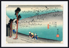 A framed Japanese-style art print depicting a coastal landscape with turquoise water, a sandy shoreline, several small figures near the bottom, and trees on the left. The print is shown with a wide white mat and a black frame against a plain white background.