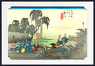 A framed Japanese ukiyo-e woodblock print showing a coastal scene with figures, trees, boats, and blue fish, presented with a white mat and black frame.