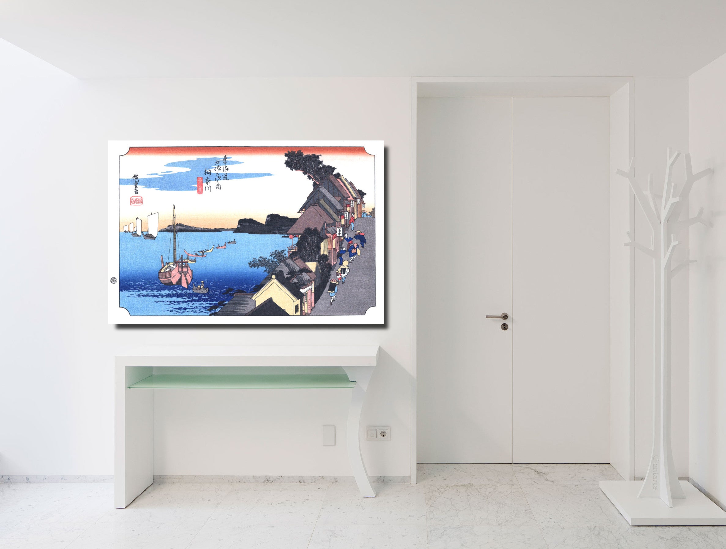 A framed art print of a Japanese ukiyo-e woodblock scene featuring a harbor with boats, displayed on a white console table in a minimalist white room.