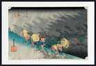 A framed Japanese ukiyo-e woodblock print showing figures walking along a path in the rain, with a wide white mat and black frame around the artwork.