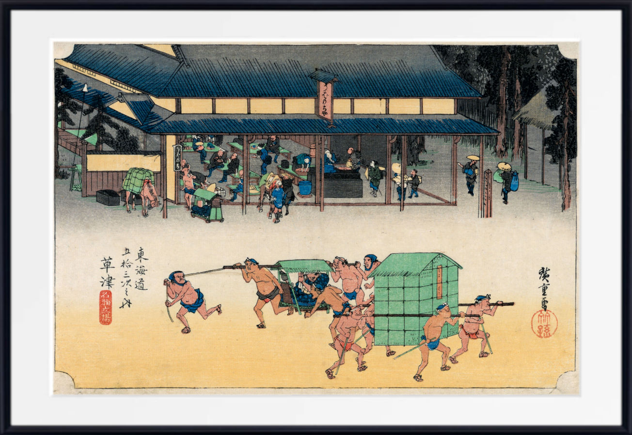 A framed Japanese ukiyo-e woodblock print depicting sumo wrestlers and a green cart in front of a temple, shown with a wide white mat and black frame.