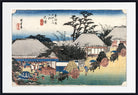 A framed Japanese ukiyo-e woodblock print showing a coastal village scene with thatched-roof houses, figures, boats, and carts, presented with a white mat and black frame.