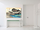 A framed art print of a Japanese ukiyo-e woodblock scene, depicting a torii gate, mountains, and blue water, displayed on a white wall above a white console table in a minimalist room.