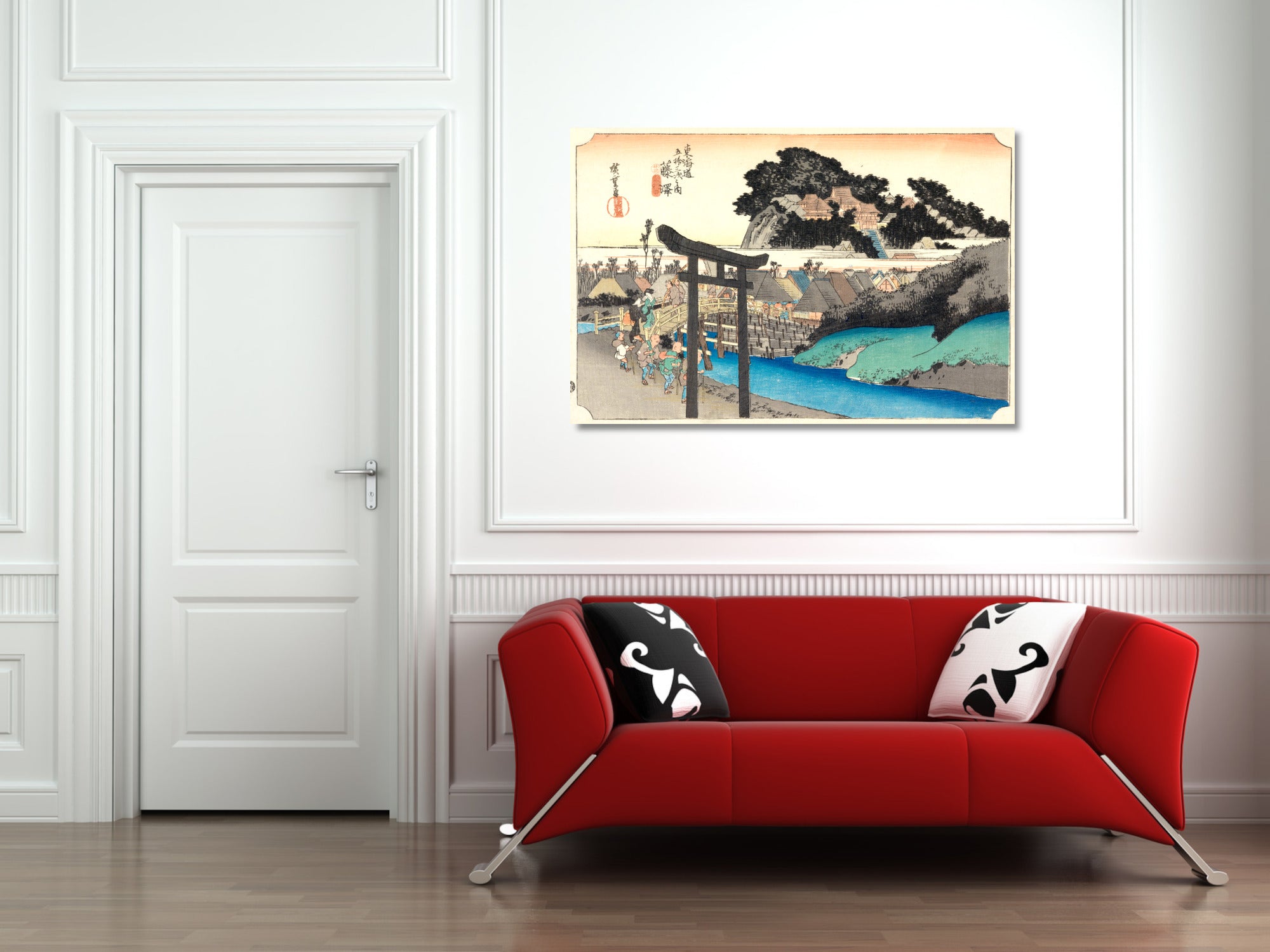 A framed Japanese-style art print depicting a scenic landscape with a torii gate, trees, and blue water, displayed on a white wall above a modern red sofa with black-and-white pillows.