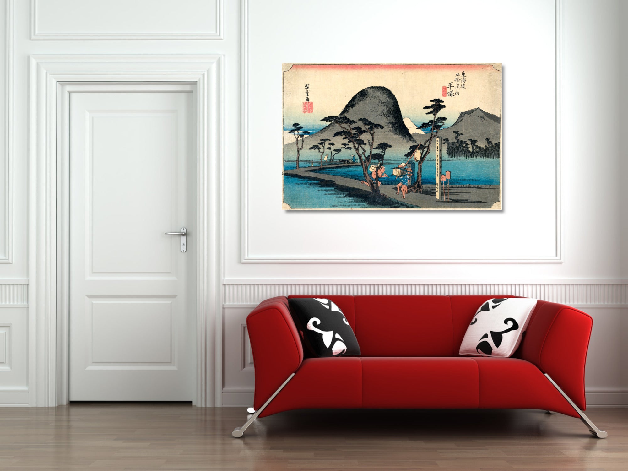 A framed Japanese-style landscape art print hangs on a white wall above a modern red sofa with black-and-white patterned pillows in a bright, minimalist room.