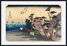 A framed Japanese ukiyo-e woodblock print depicting a rainy coastal village scene with figures, trees, houses, and blue water, shown against a white mat and black frame.