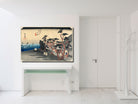 A framed Japanese ukiyo-e woodblock print depicting a rainy street scene with trees and figures, displayed on a white wall above a console table in a minimalist white interior.