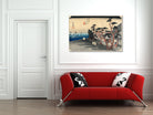 A framed Japanese ukiyo-e woodblock print depicting a rainy street scene with trees and figures, displayed on a white wall above a modern red sofa with black-and-white patterned pillows.