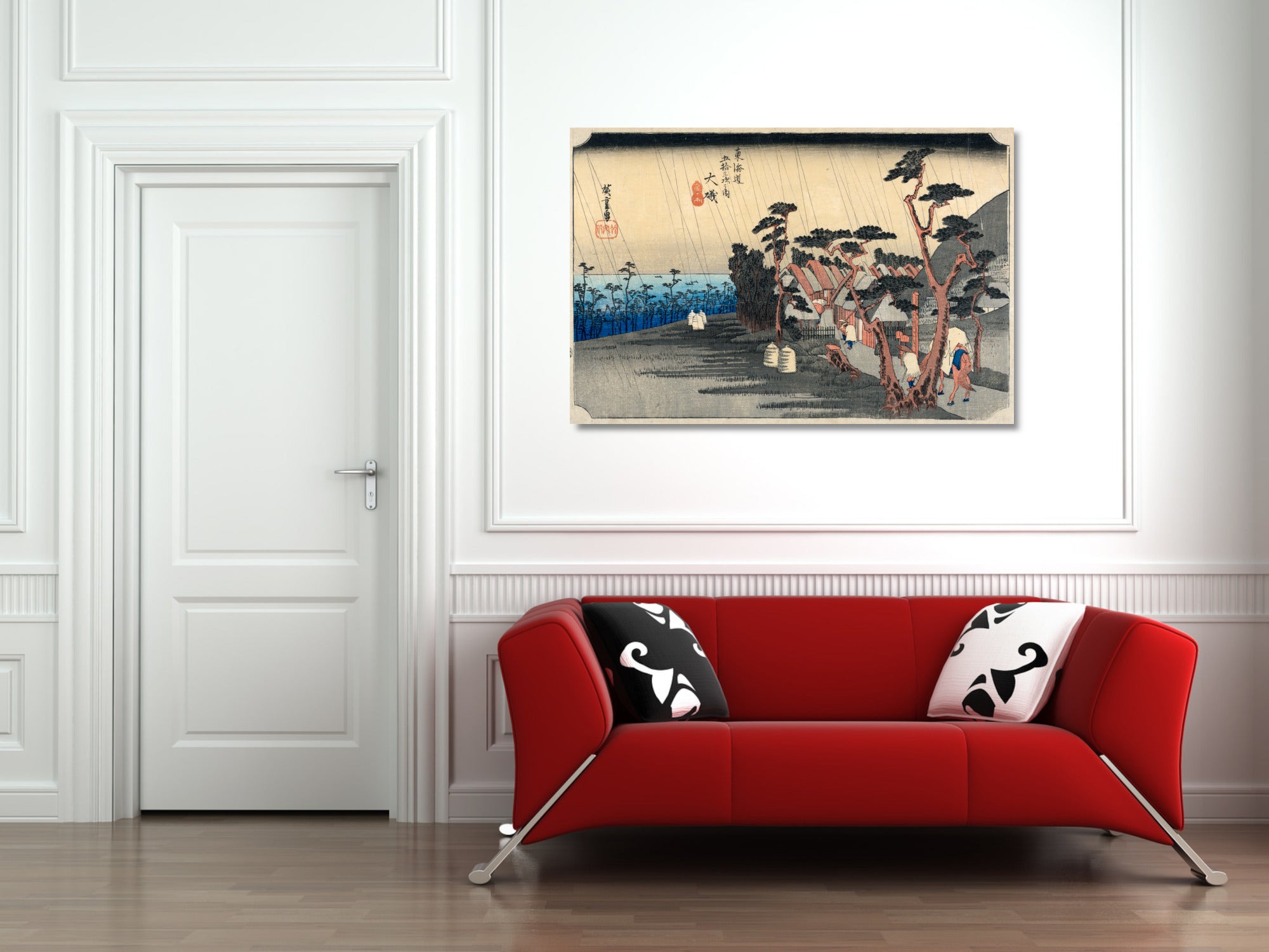 A framed Japanese ukiyo-e woodblock print depicting a rainy street scene with trees and figures, displayed on a white wall above a modern red sofa with black-and-white patterned pillows.