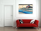 A framed Japanese-style art print depicting a scenic landscape with blue water, mountains, and a red sun, displayed on a white wall above a modern red sofa with black-and-white patterned pillows.