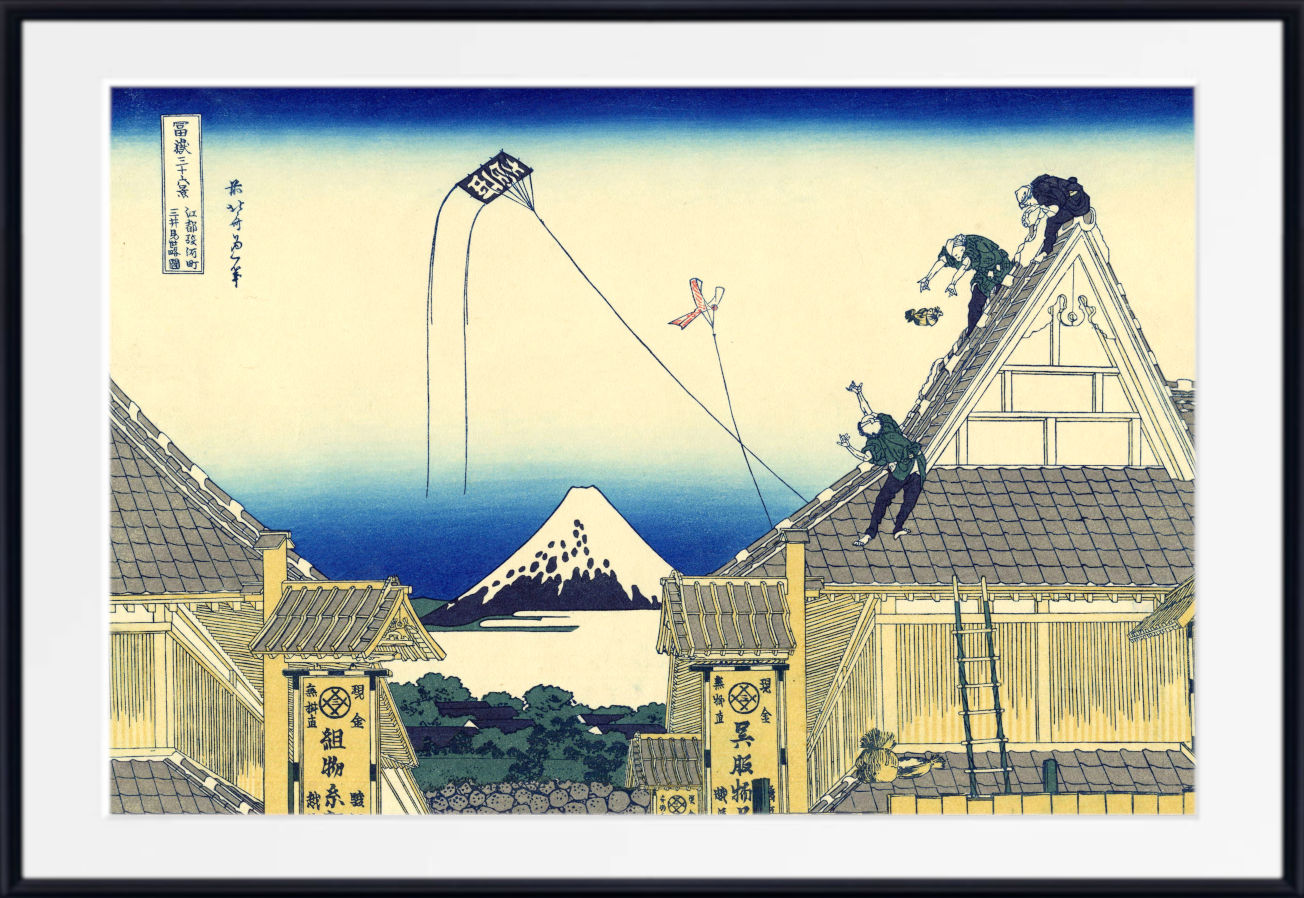 A framed Japanese-style art print depicting a village scene with rooftops, a distant mountain, and blue sky, shown against a white mat and black frame.