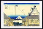 A framed Japanese-style art print depicting a village scene with rooftops, a distant mountain, and blue sky, shown against a white mat and black frame.