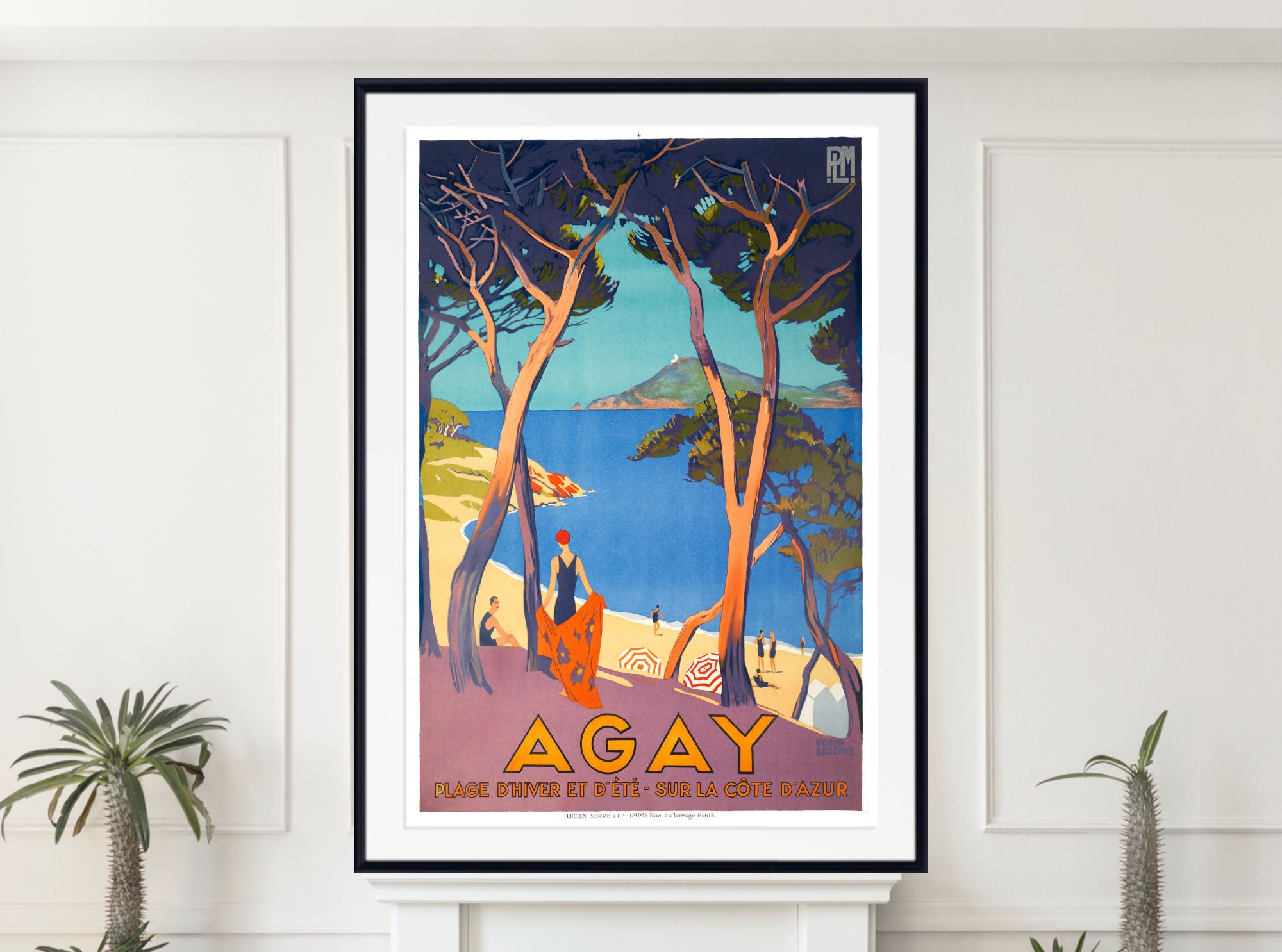 A framed vintage-style travel poster for Agay, France, displayed on a white wall above a white mantelpiece with small potted plants. The poster features an Art Deco illustration with blue water, dark trees, and a figure in orange near the beach, with the word 'AGAY' in large yellow letters at the bottom.