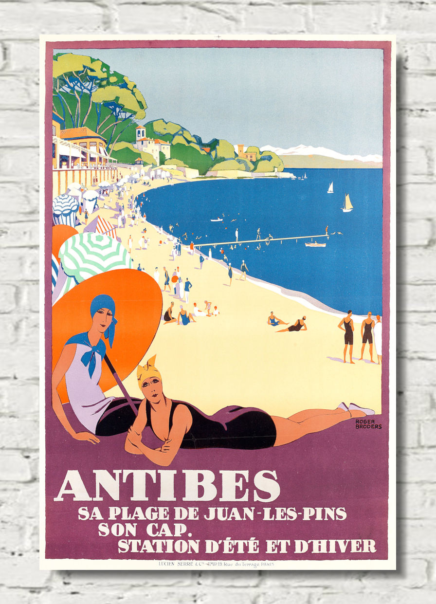 A vintage-style travel poster for Antibes beach, featuring illustrated figures on a sandy shore, a blue sea, and French text at the bottom, displayed against a white brick wall.