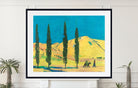 A framed art print depicting a vibrant landscape with tall cypress trees, rolling hills, and two camels under a bright blue sky, displayed on a white wall above a mantel with potted plants.