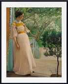 A framed art print of the classic painting 'A Girl in a Garden' by John William MacDonald, depicting a young woman in a cream dress on a wooden deck looking towards a garden path.