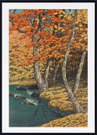 A framed art print depicting an autumn forest scene with vibrant orange and yellow foliage, a winding river, and dark rocks, presented in a black frame with a white mat.