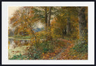 A framed landscape art print depicting an autumn forest scene with a path, trees, and a reflective pond, shown with a white mat and black frame.