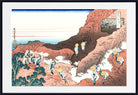 A framed Japanese-style art print depicting a coastal mountain scene with figures walking along a path, shown against a white mat and black frame.
