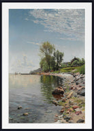 A framed landscape art print depicting a calm lake shoreline with trees, rocks, a small house, and a cloudy blue sky, shown with a white mat and black frame.