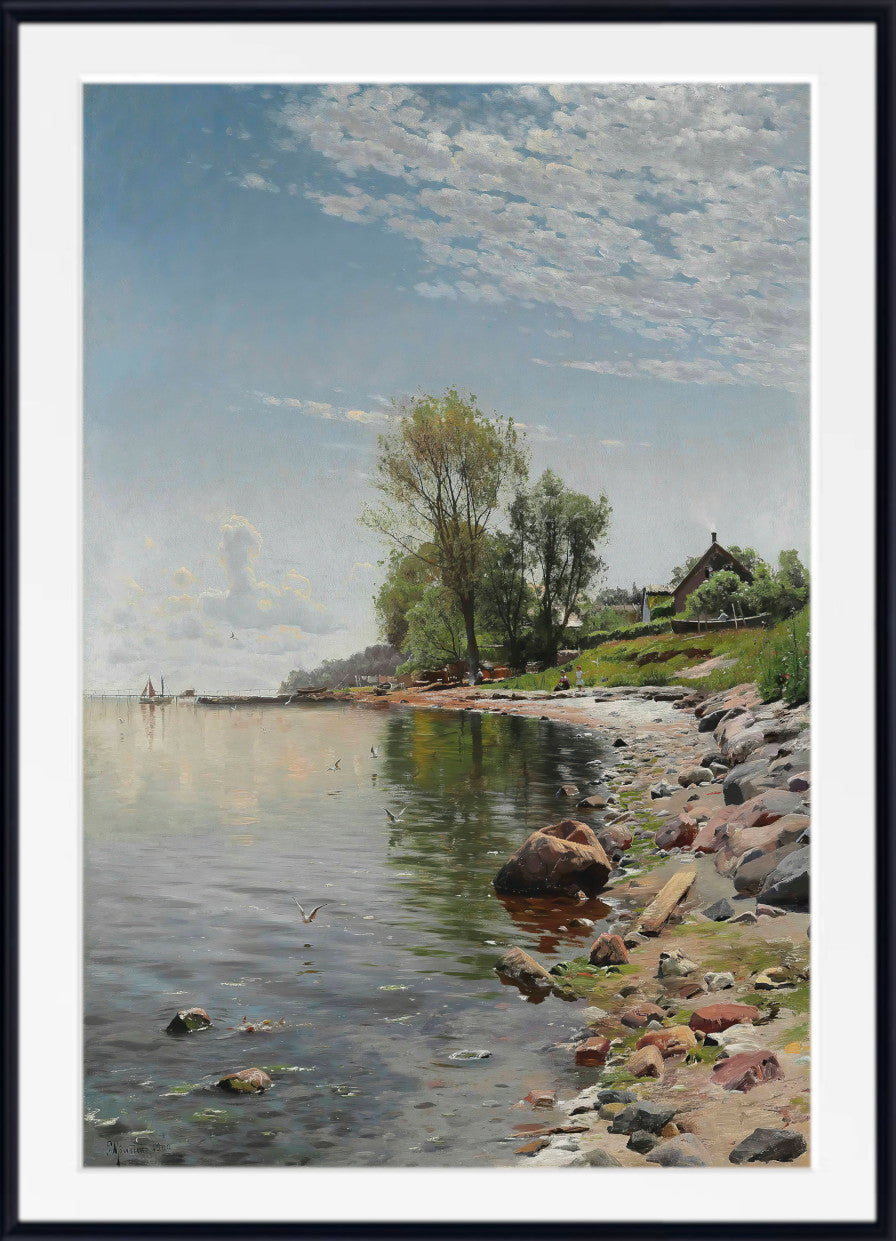A framed landscape art print depicting a calm lake shoreline with trees, rocks, a small house, and a cloudy blue sky, shown with a white mat and black frame.
