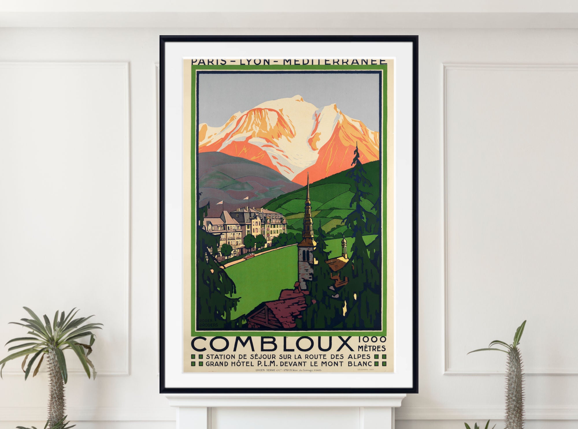 A framed vintage-style travel poster of Combloux, Switzerland, hanging on a white wall above a mantel, flanked by small potted plants. The poster features a retro illustration of a mountain, green valley, and buildings, with the text 'PARIS - LYON - MEDITERRANEE' at the top and 'COMBLOUX 1966' at the bottom.