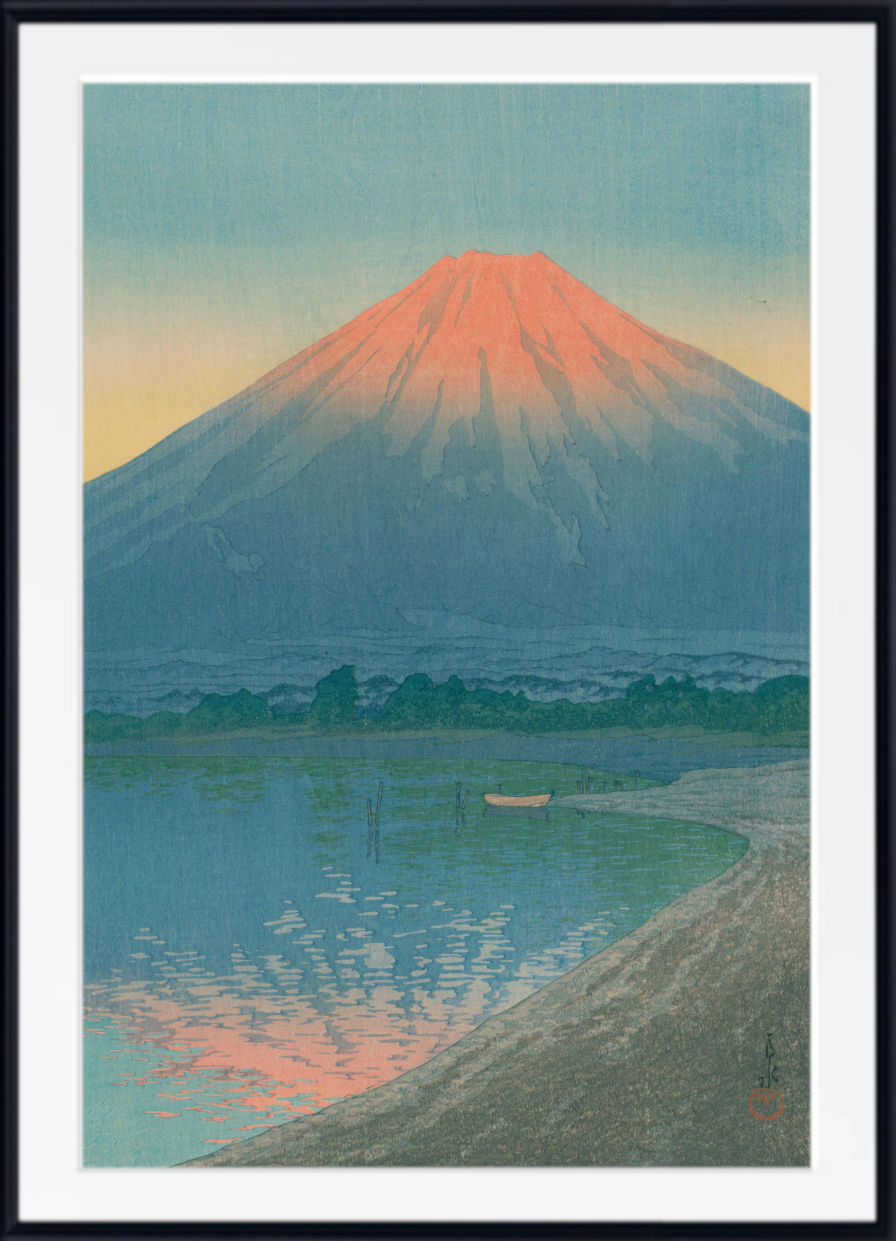 A framed art print depicting Mount Fuji with a warm pink-orange sky and reflections in the water, shown with a white mat and black frame.