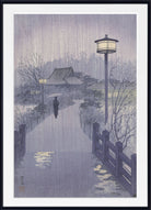 A framed Japanese-style art print depicting a rainy scene with a pathway, lanterns, bare trees, and a small house, shown against a white background with a black frame.