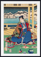 A framed Japanese ukiyo-e woodblock print depicting a seated woman in a blue and red kimono indoors, with a snowy outdoor scene visible through the window behind her. The print is shown with a white mat and black frame.