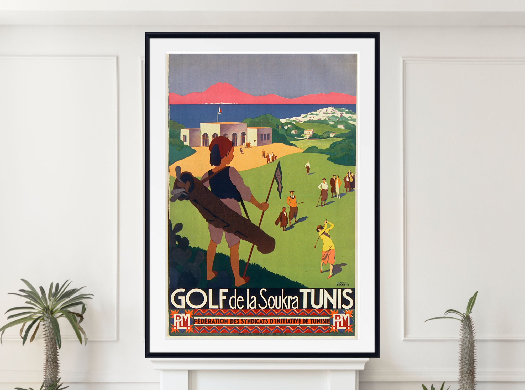 A framed vintage-style travel poster for 'GOLF de la Soukra TUNIS' hangs on a white wall above a mantel, flanked by small potted plants. The poster features retro illustration art of people playing golf on a green hillside with mountains and a pink sky in the background.