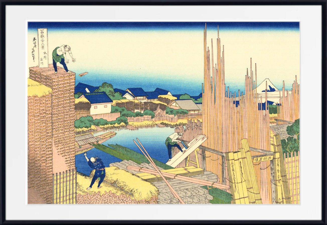 A framed Japanese ukiyo-e woodblock print showing workers constructing a brick wall beside a pond, with houses and bamboo in the background. The print is presented with a white mat and a black frame.