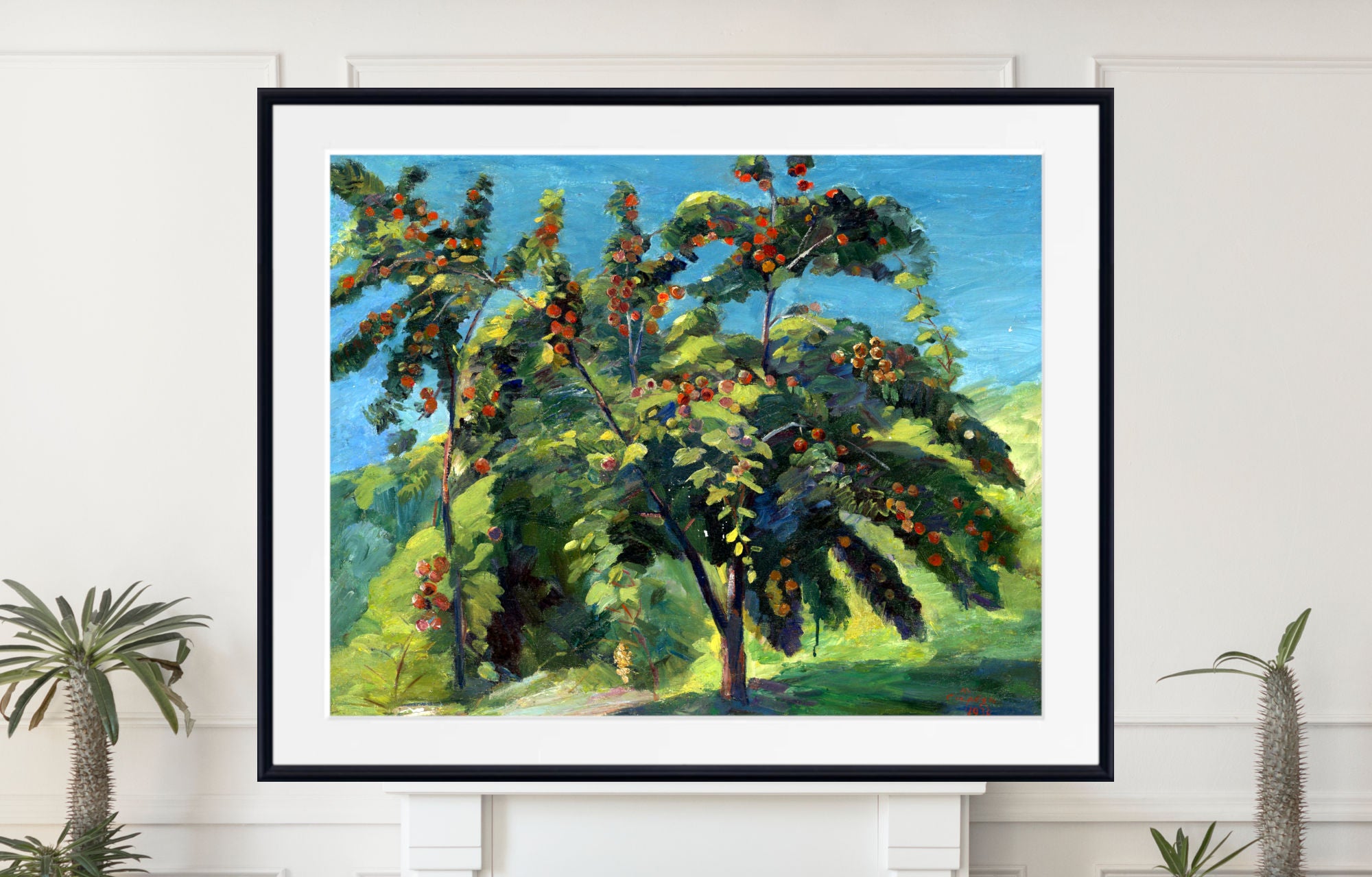 A framed landscape painting of leafy green trees with red and orange fruits under a bright blue sky, displayed on a white wall above a mantel with potted plants.