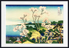 A framed Japanese ukiyo-e woodblock print depicting a coastal landscape with Mount Fuji, flowering trees, figures walking along a path, and buildings near the water. The print is shown with a white mat and a black frame against a light gray background.