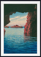 A framed art print depicting a scenic coastal view from within a rocky cave, looking out over calm blue water toward distant islands under a pale sky. The print has a wide white mat and a black frame.