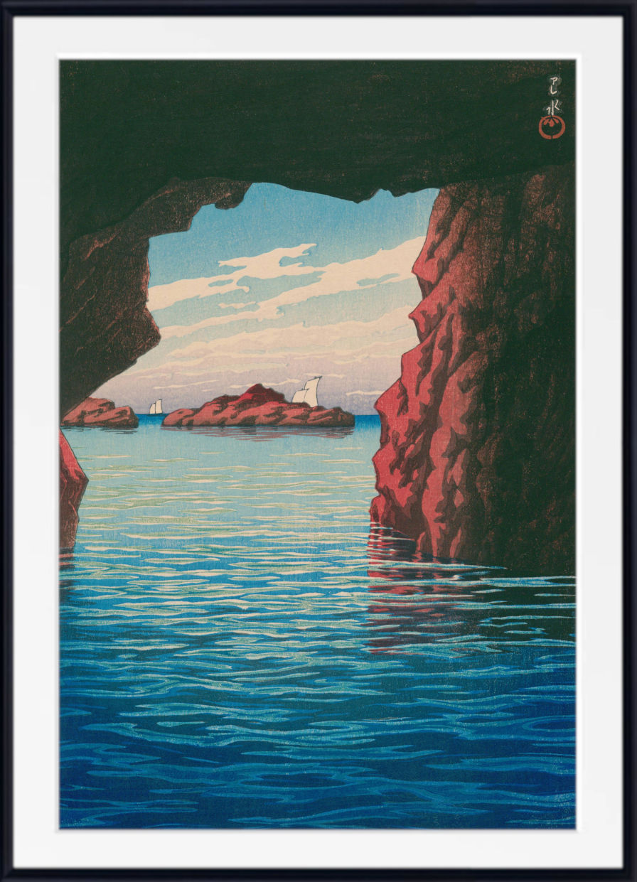 A framed art print depicting a scenic coastal view from within a rocky cave, looking out over calm blue water toward distant islands under a pale sky. The print has a wide white mat and a black frame.