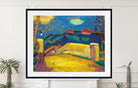 A framed art print featuring an impressionist landscape painting with vibrant yellow fields, deep blue mountains, and purple sky, displayed on a white wall above a mantel with small potted plants. Alexej von Jawlensky – Landschaft mit Brücke, circa 1909