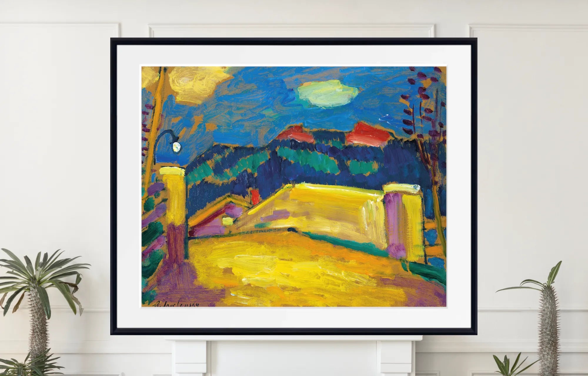A framed art print featuring an impressionist landscape painting with vibrant yellow fields, deep blue mountains, and purple sky, displayed on a white wall above a mantel with small potted plants. Alexej von Jawlensky – Landschaft mit Brücke, circa 1909