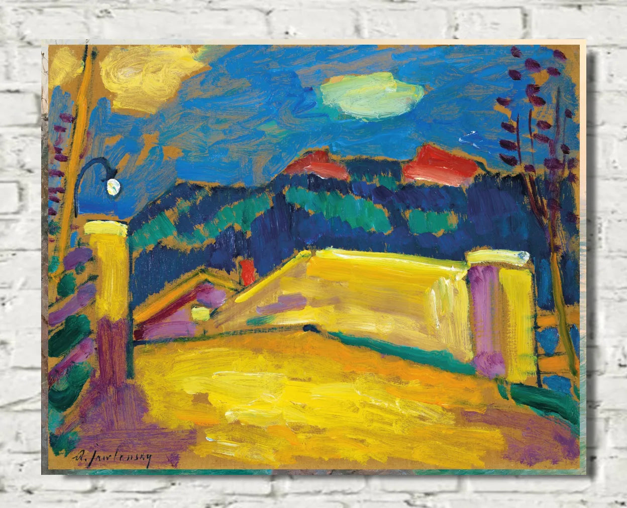 An expressionist landscape painting on canvas, featuring a vibrant yellow foreground, dark blue mountains, and a swirling blue sky, mounted on a white brick wall.  Alexej von Jawlensky – Landschaft mit Brücke, circa 1909