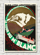 A vintage-style travel poster for a mountain cycling tour, featuring bold French text, illustrated mountains, a small village with a church spire, and a vintage car in the foreground. The poster is displayed against a light gray brick wall background.