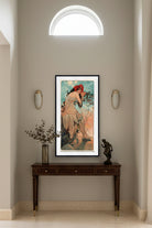 A framed vintage Art Nouveau style print featuring a seated woman in flowing pale drapery, with a red flower crown, against a sky-like background in blue, peach, and orange tones.