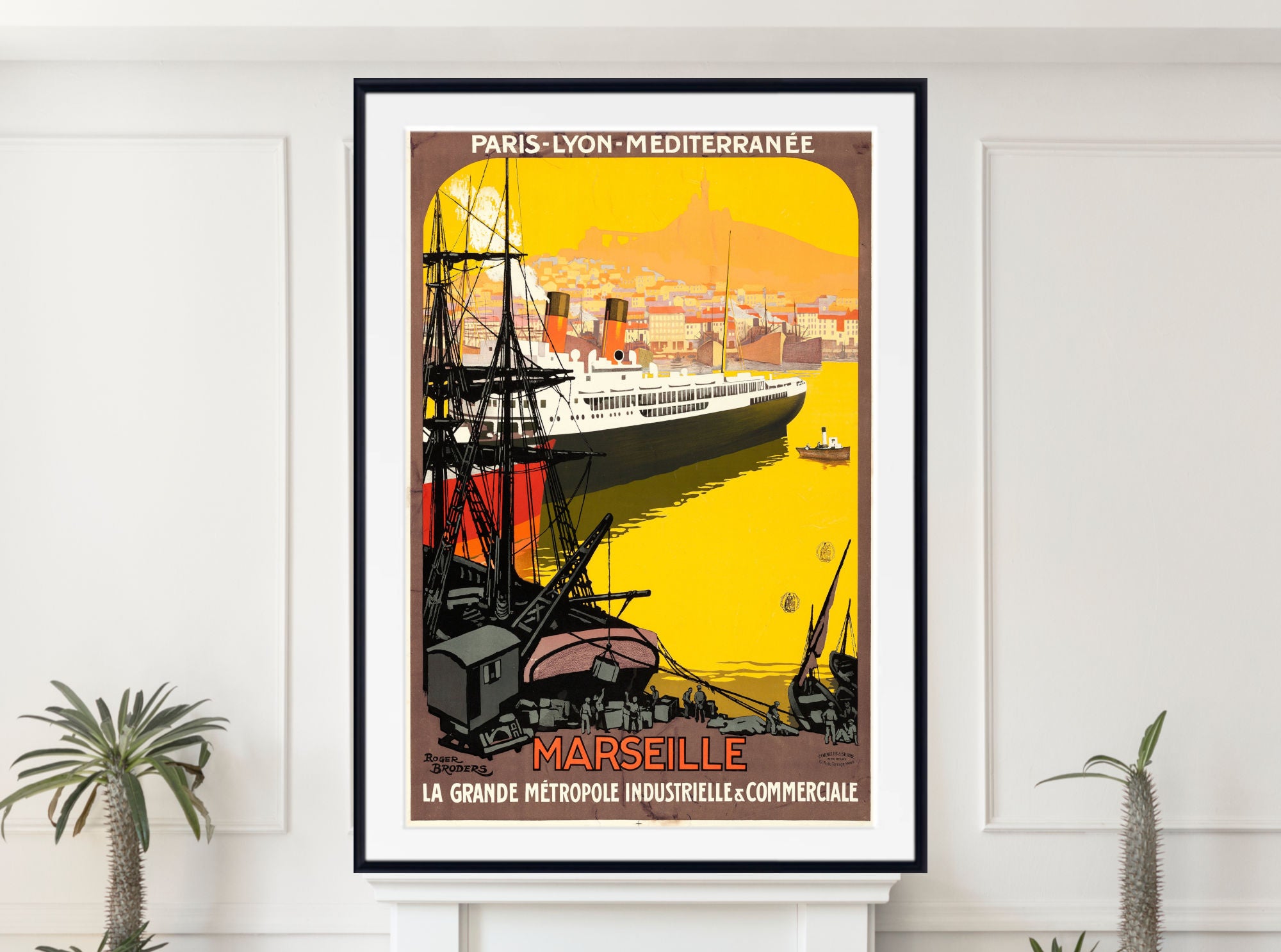 A framed vintage-style travel poster for Marseille, Paris-Lyon-Méditerranée, displayed on a white wall above a mantel with small potted plants. The poster features a large white ocean liner on a bright yellow harbor scene with black ships and warm orange-brown city tones.