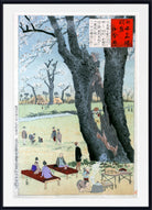 A framed Japanese woodblock-style art print depicting a park scene with large dark trees, blooming cherry blossoms, people sitting and walking, and a red text panel in the upper right. The print is shown with a white mat and black frame.