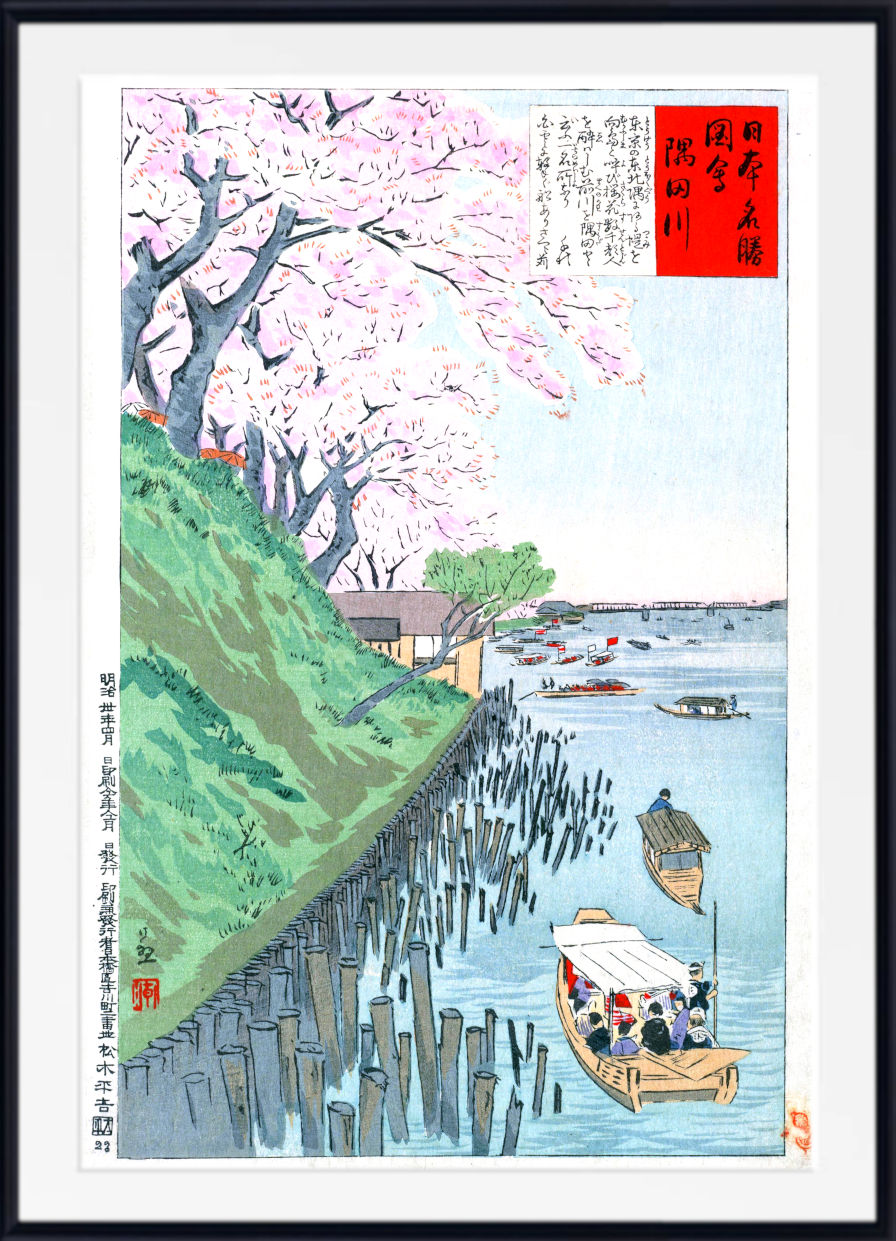 A framed Japanese ukiyo-e woodblock print depicting a scenic river or harbor with pink cherry blossoms, a green hillside, wooden boats, and Japanese text panels, shown against a white background with a black frame.