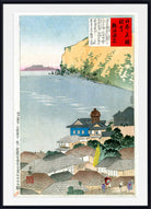 A framed Japanese ukiyo-e woodblock print depicting a coastal town with rooftops, a blue body of water, a pale yellow cliff, and a red title panel with Japanese text.