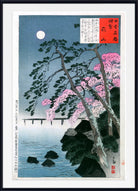 A framed Japanese ukiyo-e woodblock print depicting a moonlit scene with pink cherry blossoms, dark rocks, a bridge over water, and a blue sky. The print includes a white mat and a black frame.