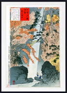 A framed Japanese ukiyo-e woodblock print depicting a waterfall flowing between rocky cliffs, with autumn-colored trees and two small figures near the base. The print is shown with a white mat and a black frame.