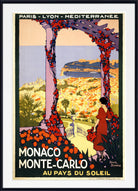 A vintage-style travel poster for Monaco and Monte-Carlo, framed with a white mat and black frame. The artwork shows a woman in a red dress standing beneath a floral archway overlooking a sunlit coastal city with blue water.